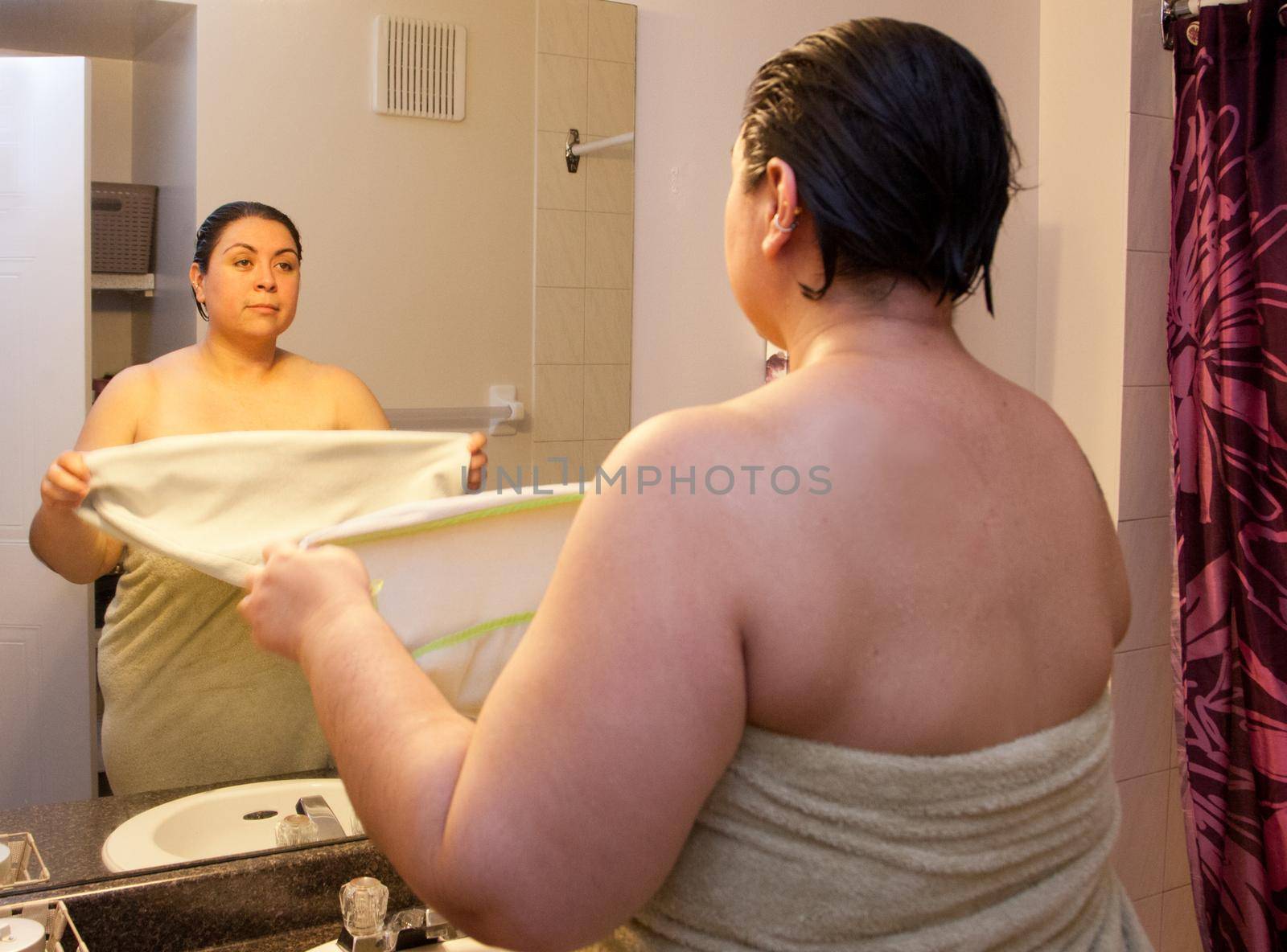 Woman stands in front of reflection as part of morning shower routine, ready to towel dry hair 