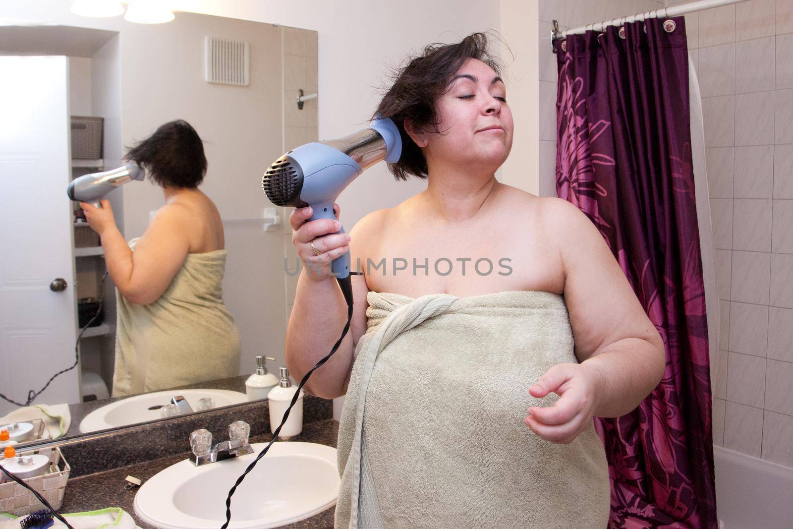 Drying hair wrapped in a towel, a woman stands in her bathroom preparing to go out 