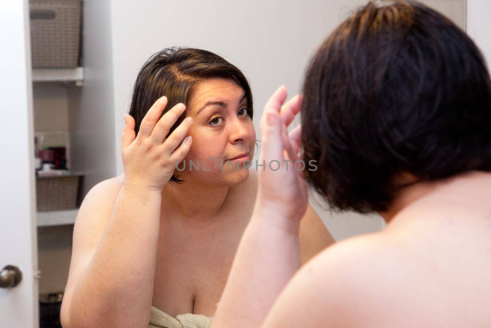 Woman looks into her mirror and touches hair 