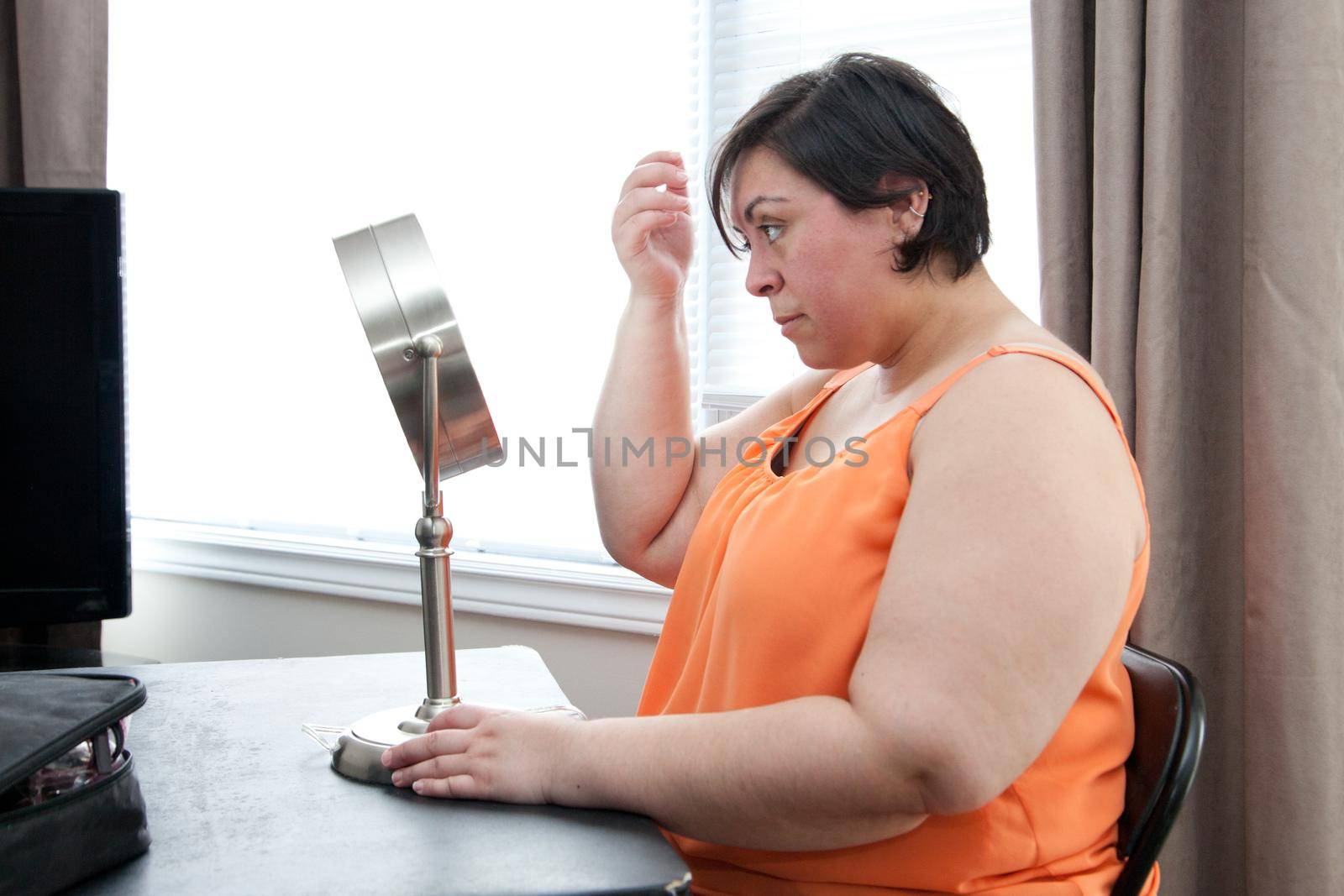 A curvy woman looks at her reflection and hair in a table top mirror