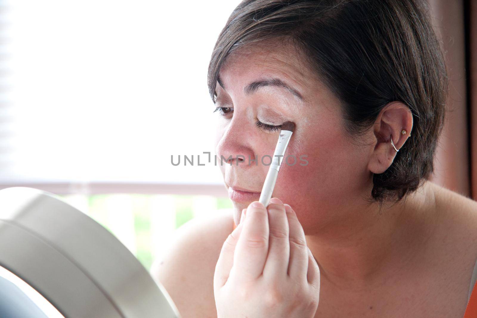 Woman in front of vanity mirror uses a makeup wand to apply eye shadow 