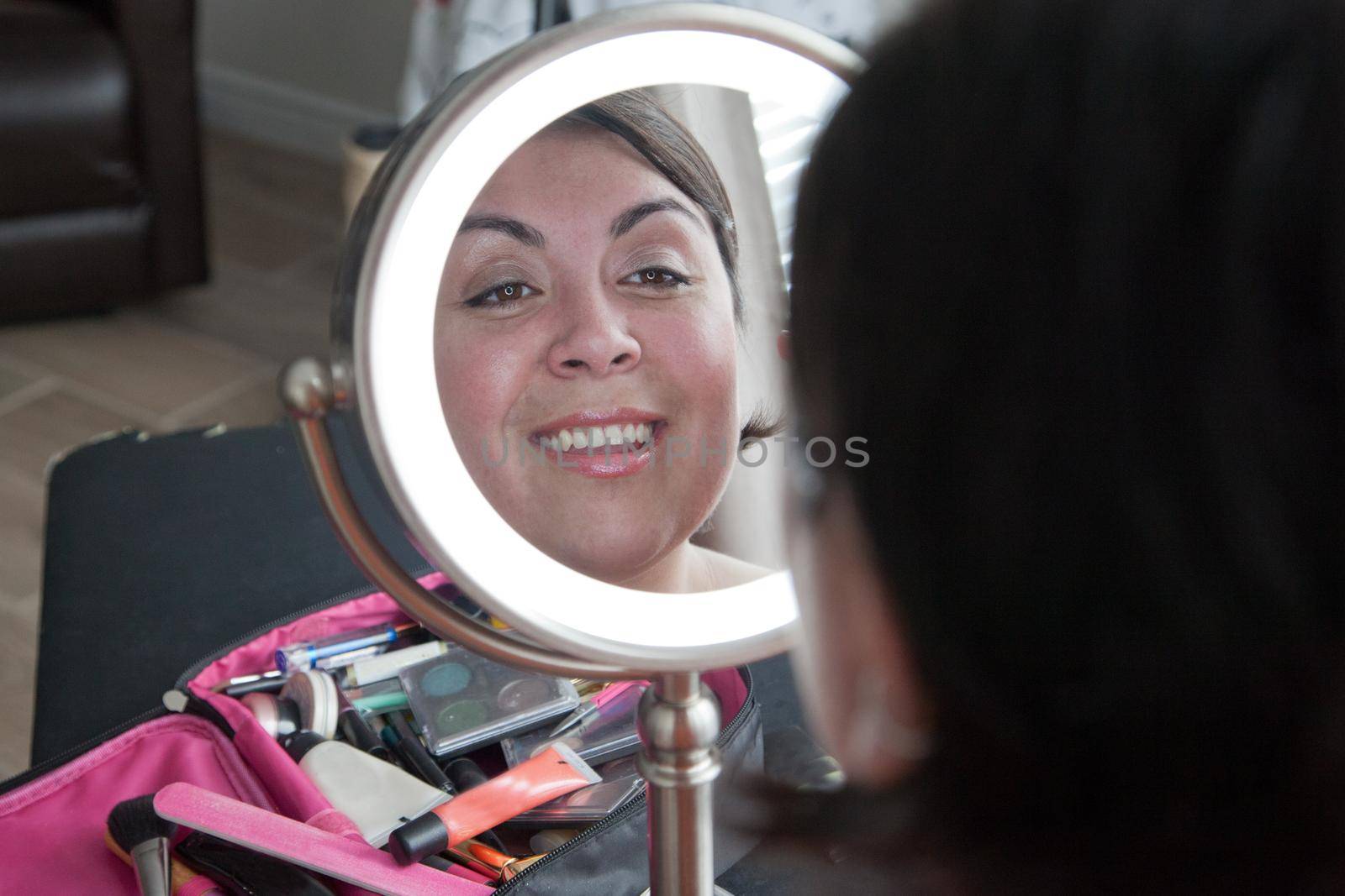Latina woman with beautiful makeup smiles at her reflection in a mirror 