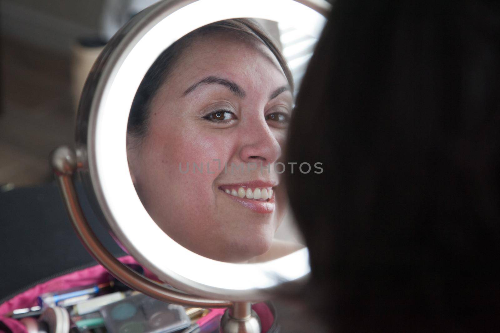 Beautiful woman smiles at her reflection in a lit mirror 