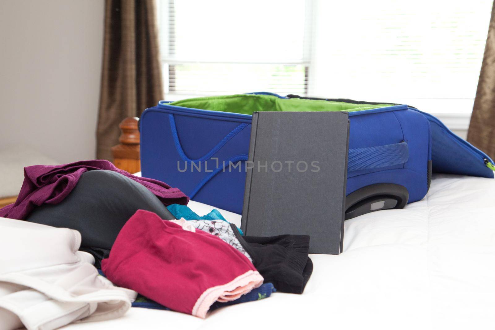 A pile of personal items on a bed beside a waiting suitcase 