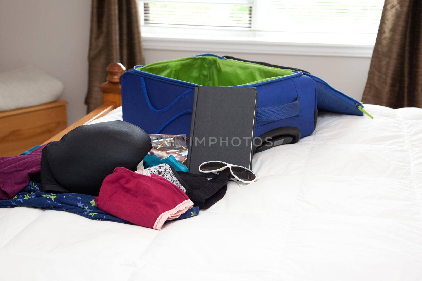 A blue suitcase is open on a bed, ready to be packed with undergarments and books for a trip 