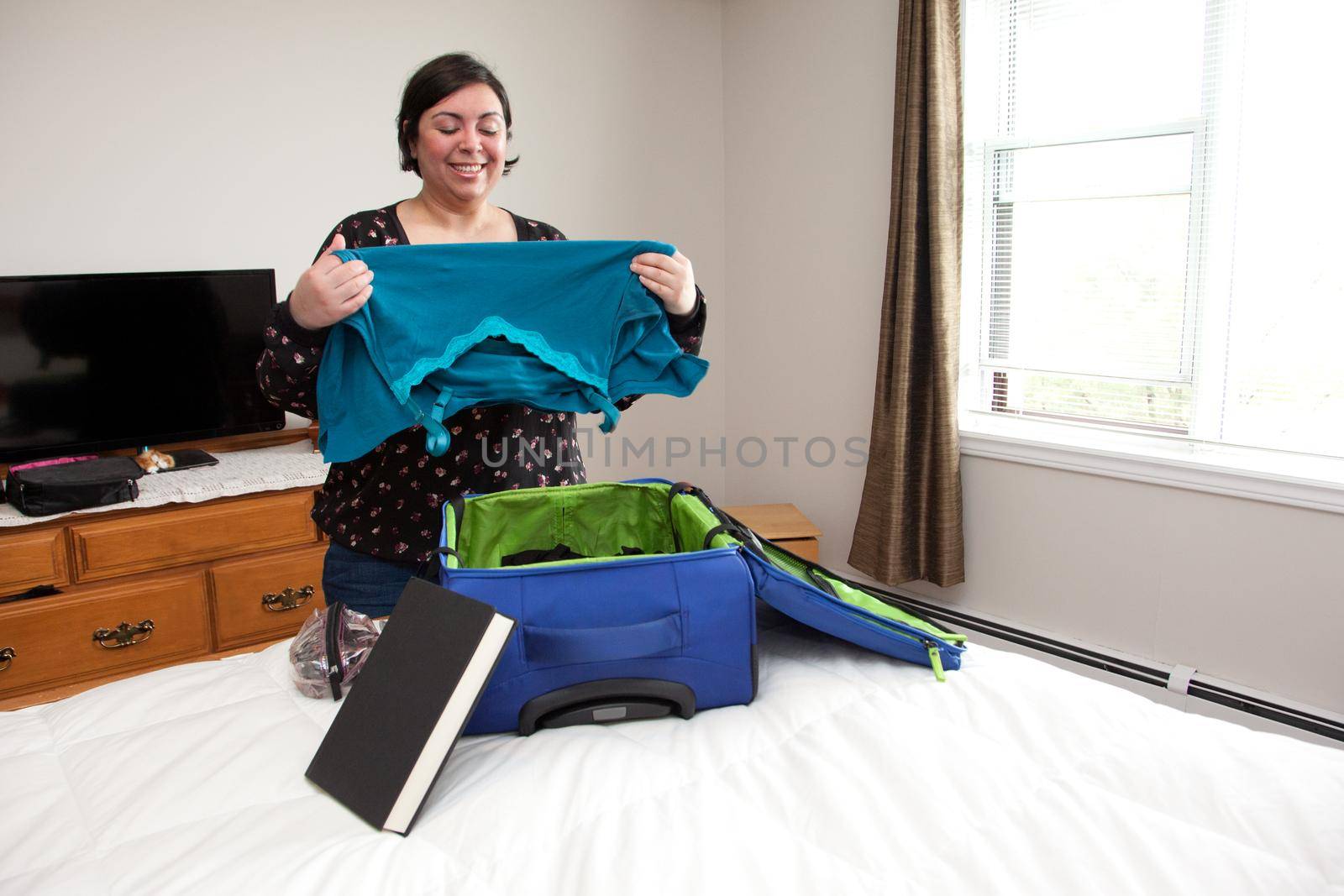 Happy smiling woman packs clothes into her suitcase for a journey 