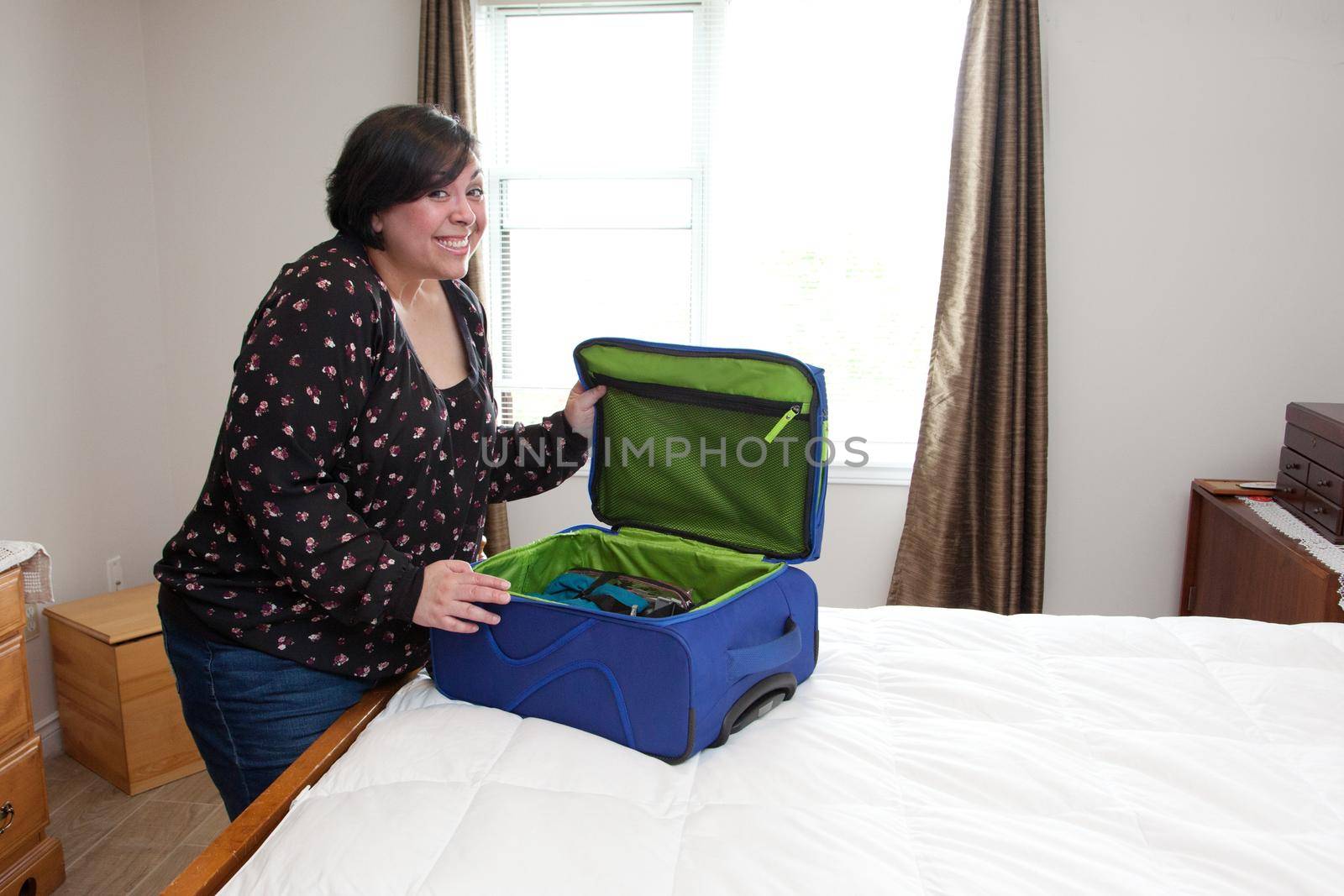 A woman smiles excitedly as she closes up her packed suitcase 