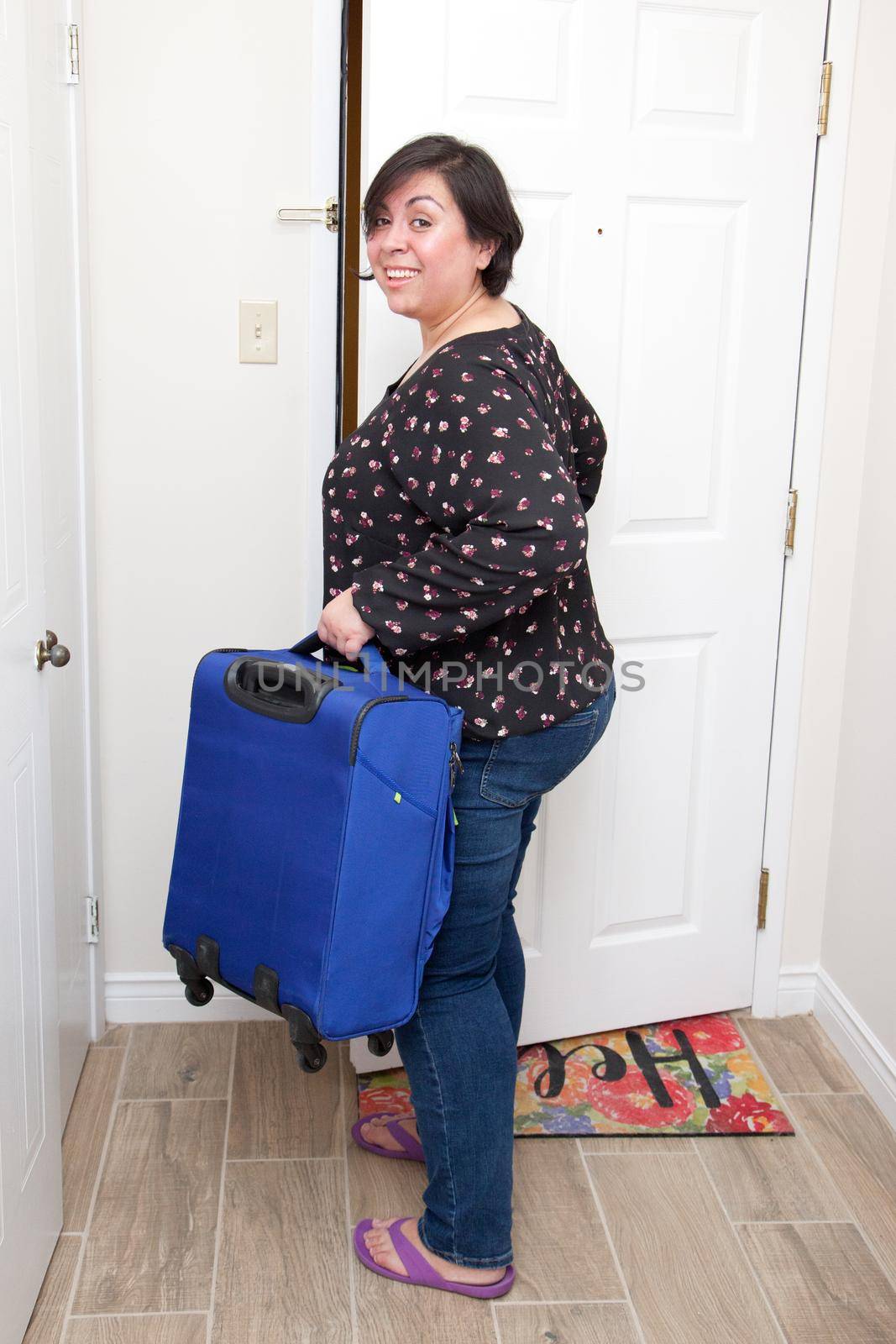  A woman holds her suitcase as she leaves her apartment or house with a smile on her face 