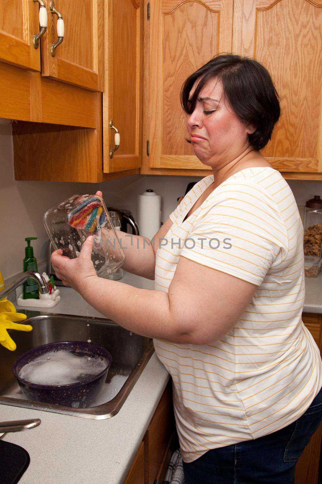 Woman makes a disgusted face as she cleans a glass dish in the kitchen 