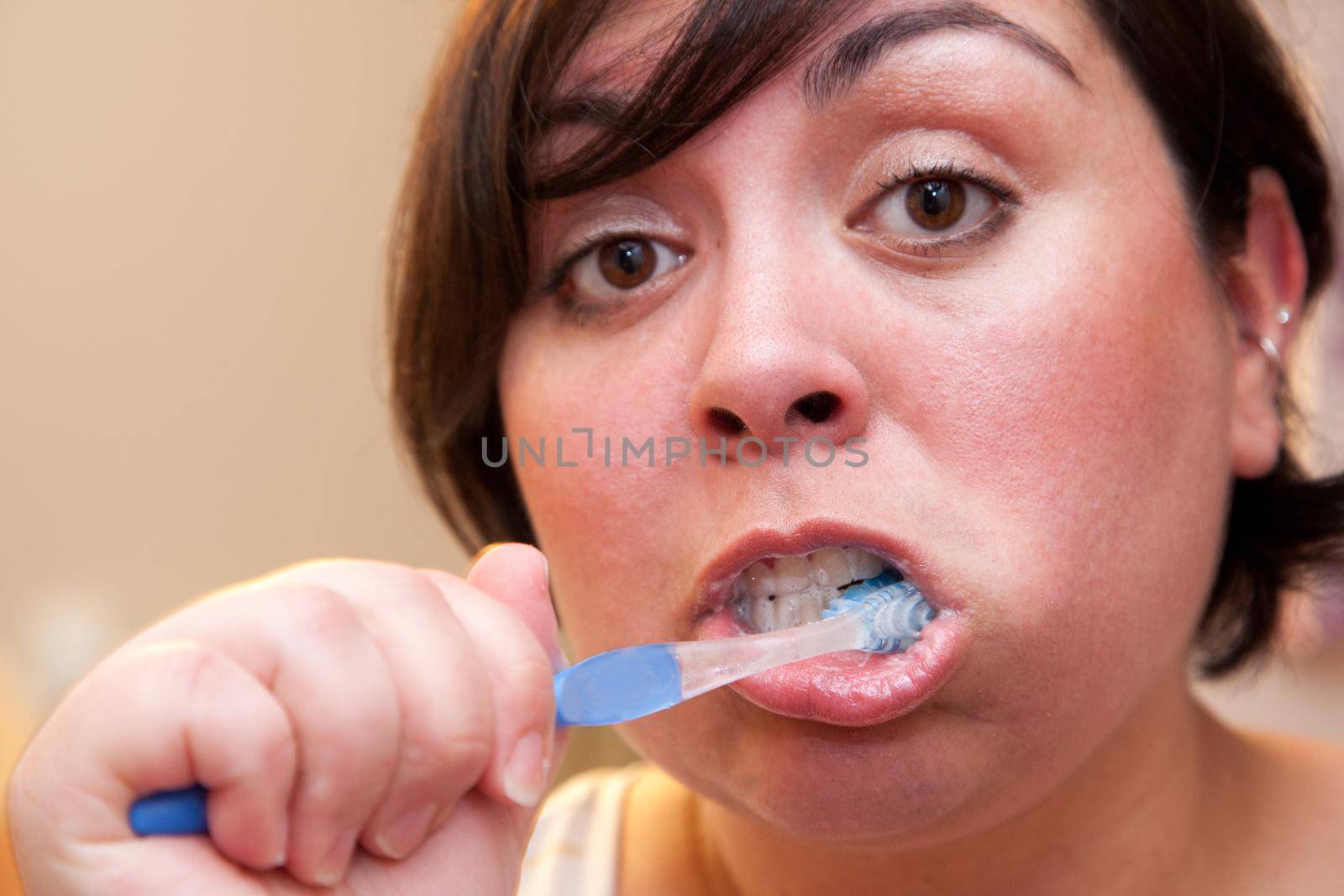 A very close to the face portrait of a woman brushing her teeth looking surprised 