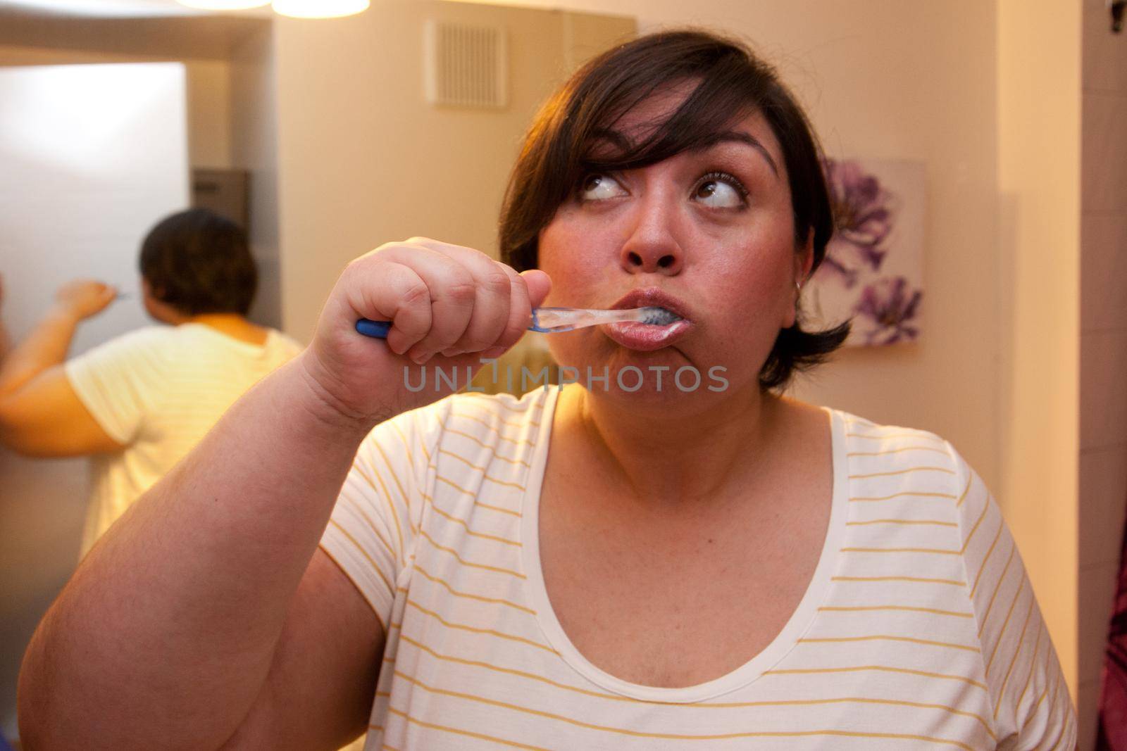 A woman brushes her teeth in the bathroom and raises her eyes in thought 