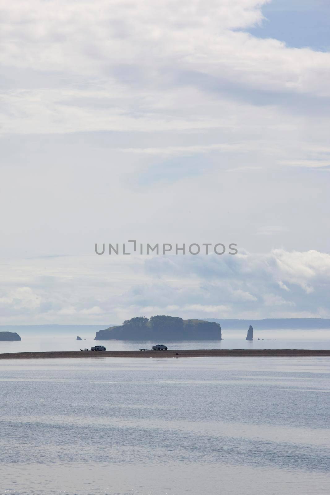 two trucks explore a hazey morning on a beach with islands behind 