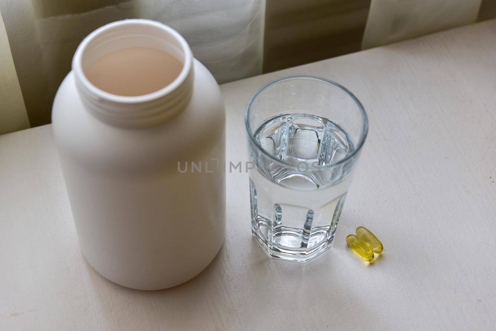 Omega-3, spirulina, chlorophyll capsules and glass of water on white wooden table. Dietary supplements, biologically active additives. vitamin pills. Health support.
