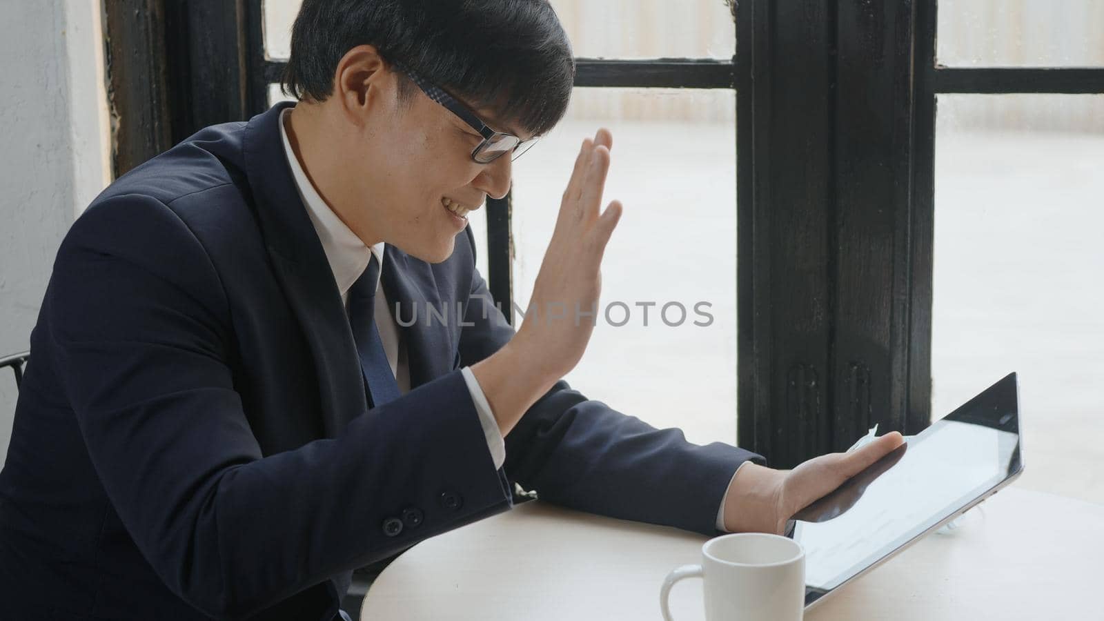 Asian businessman smiling talking through video call  by digital tablet computer in coffee shop, business man laughing doing online video chat calling conference to partners