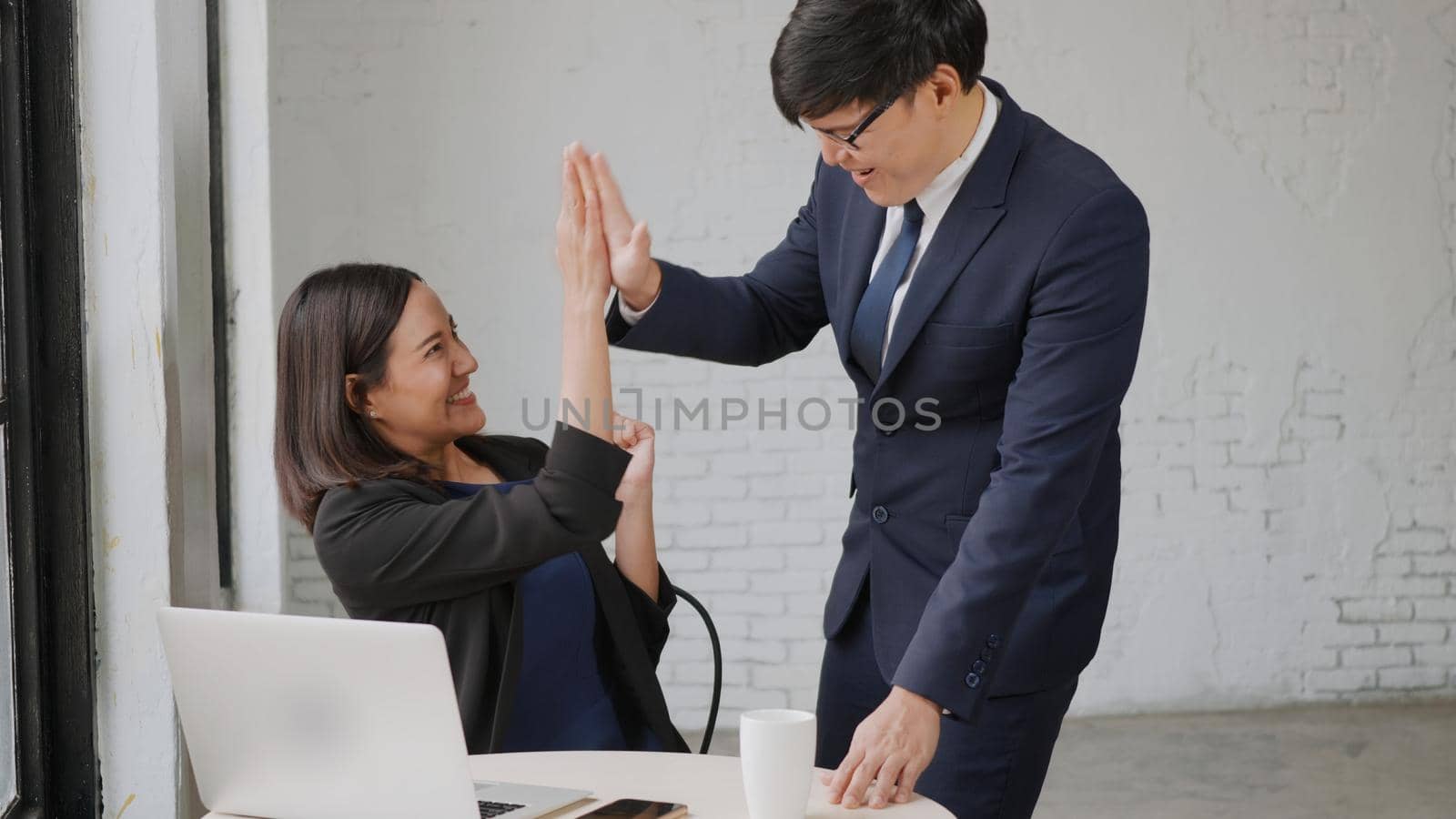 businessman and woman smile workstation triumphing with raised hands together with laptop by Sorapop