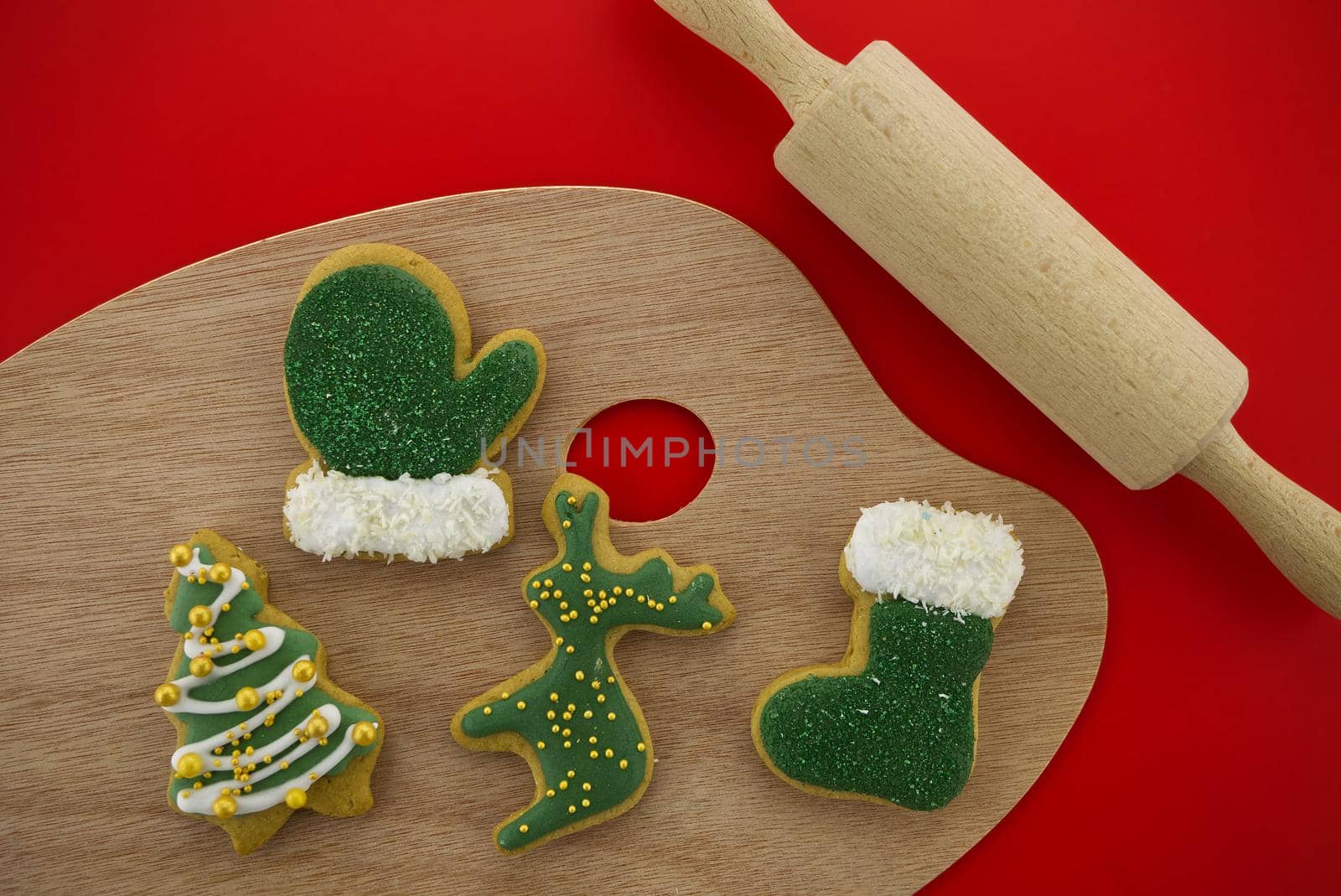 Christmas food and baking concept with a selection of colorful glazed or iced cookies in different shapes on a board with rolling pen over a festive red background in a flat lay still life
