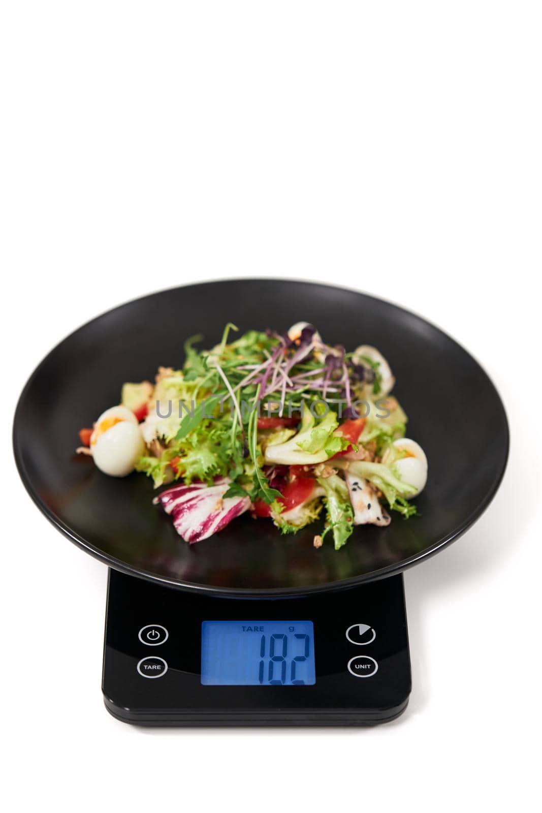 Close up of appetizing vegetables salad on black kitchen scales on white background. Concept of proper and balanced nutrition and weight of food. 