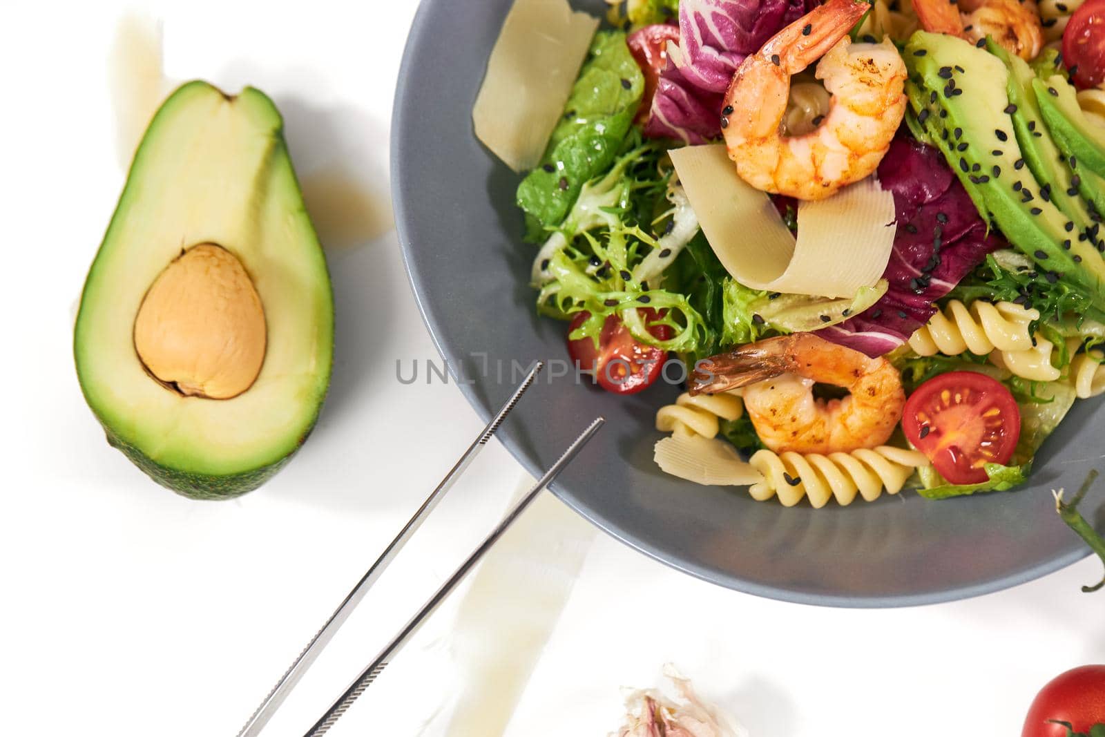 Top view close up of healthy and appetizing pasta with shrimps,tomatoes,avocado and herbs on white background. Concept of delicious dish with healthy ingredients for body weight maintenance.
