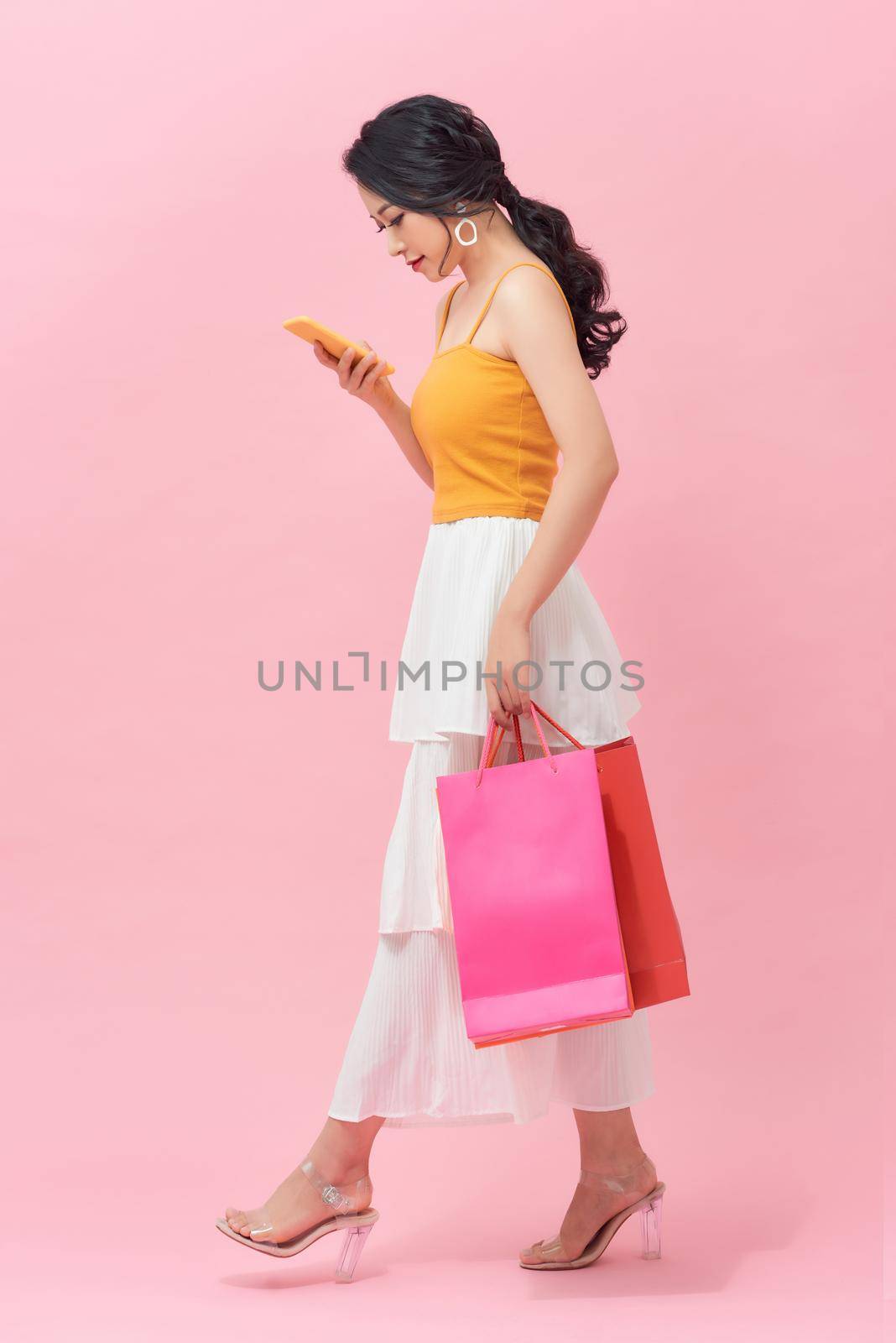 Woman carrying shopping bags and text messaging on the phone by makidotvn