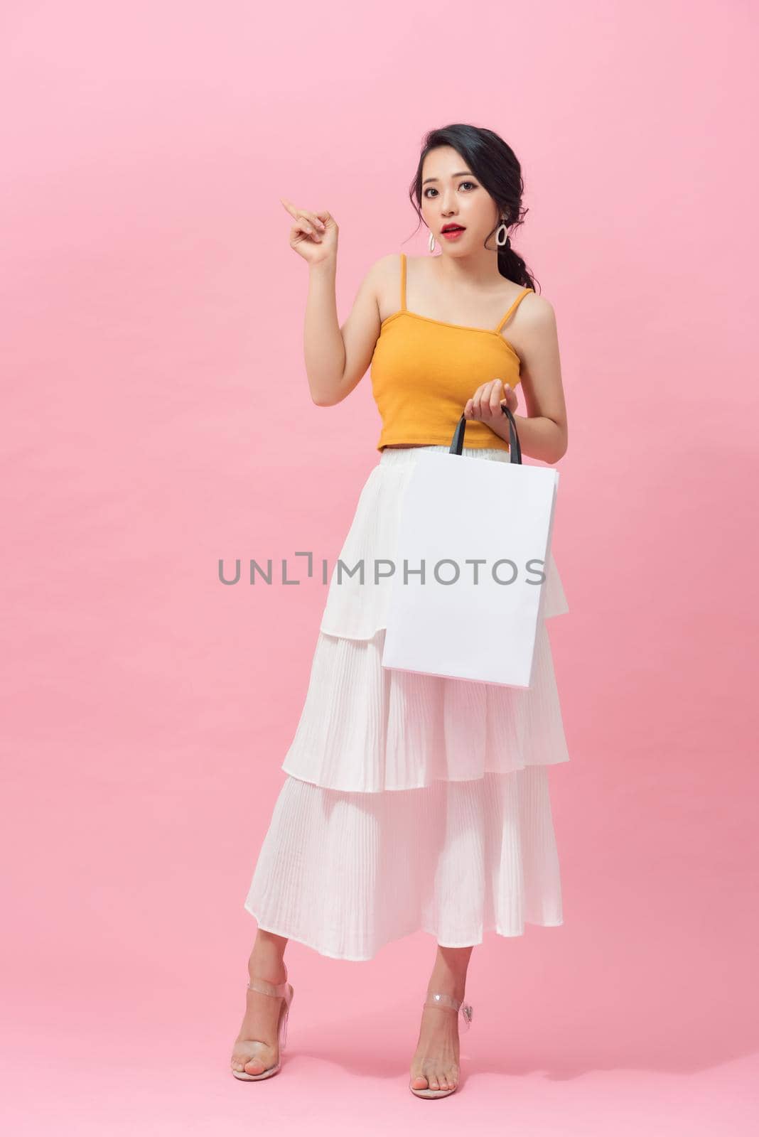 Full length portrait of smiling young woman with shopping bags over pink background. by makidotvn