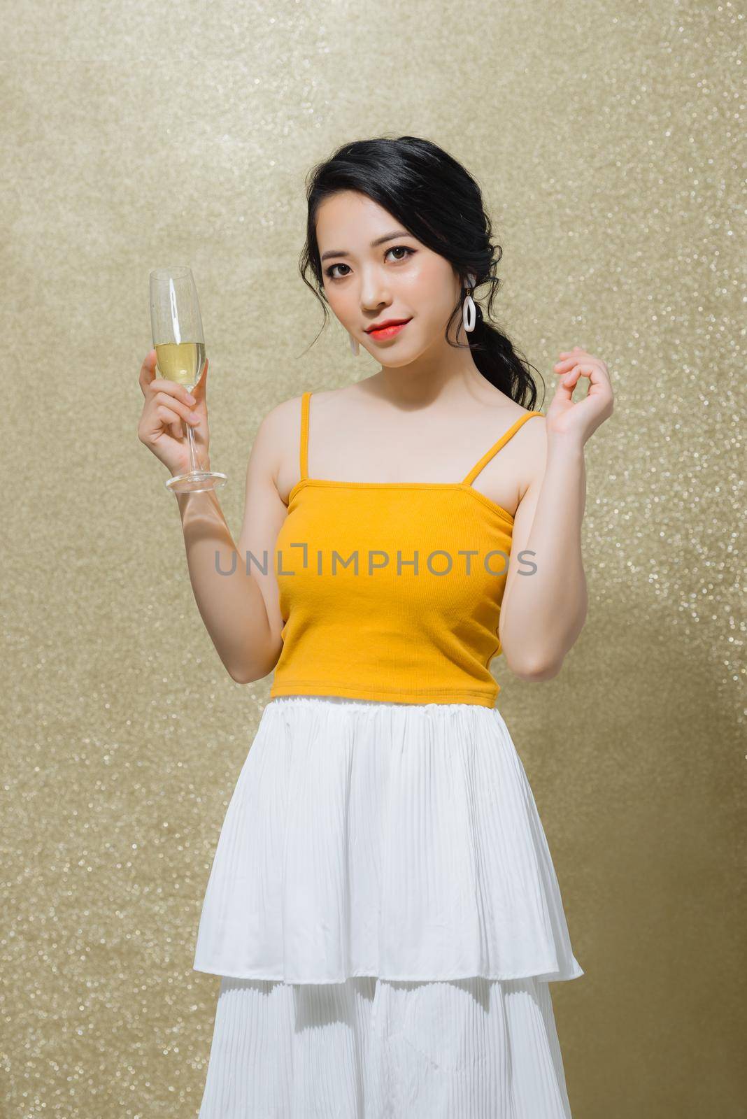 Portrait of beautiful young Asian woman holding wine glass over gold background. Celebrating concept. by makidotvn
