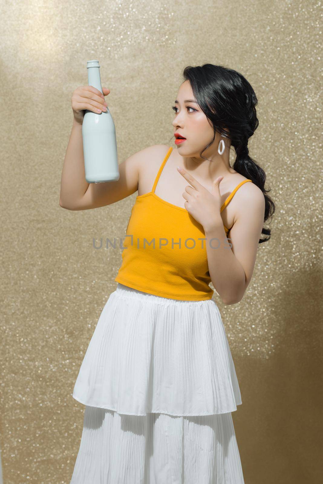 Young Asian woman holding wine bottle isolated over color background. Party, birthday, christmas concept.