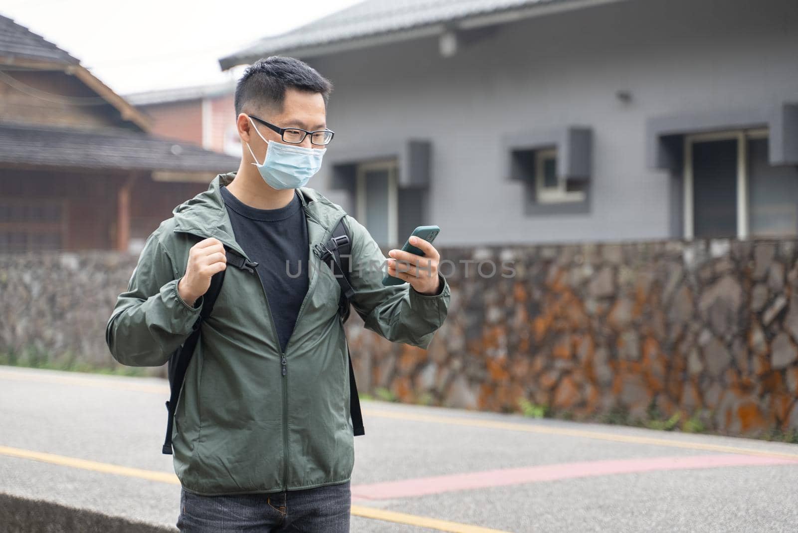 Young backpacker man is traveling alone and using smart phone with wearing mask, glasses. by ROMIXIMAGE