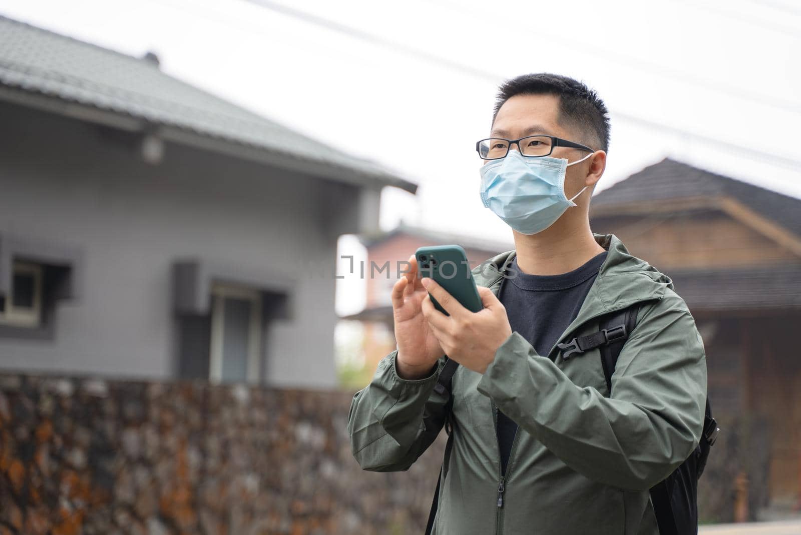 Young backpacker man is traveling alone and using smart phone with wearing mask, glasses. by ROMIXIMAGE