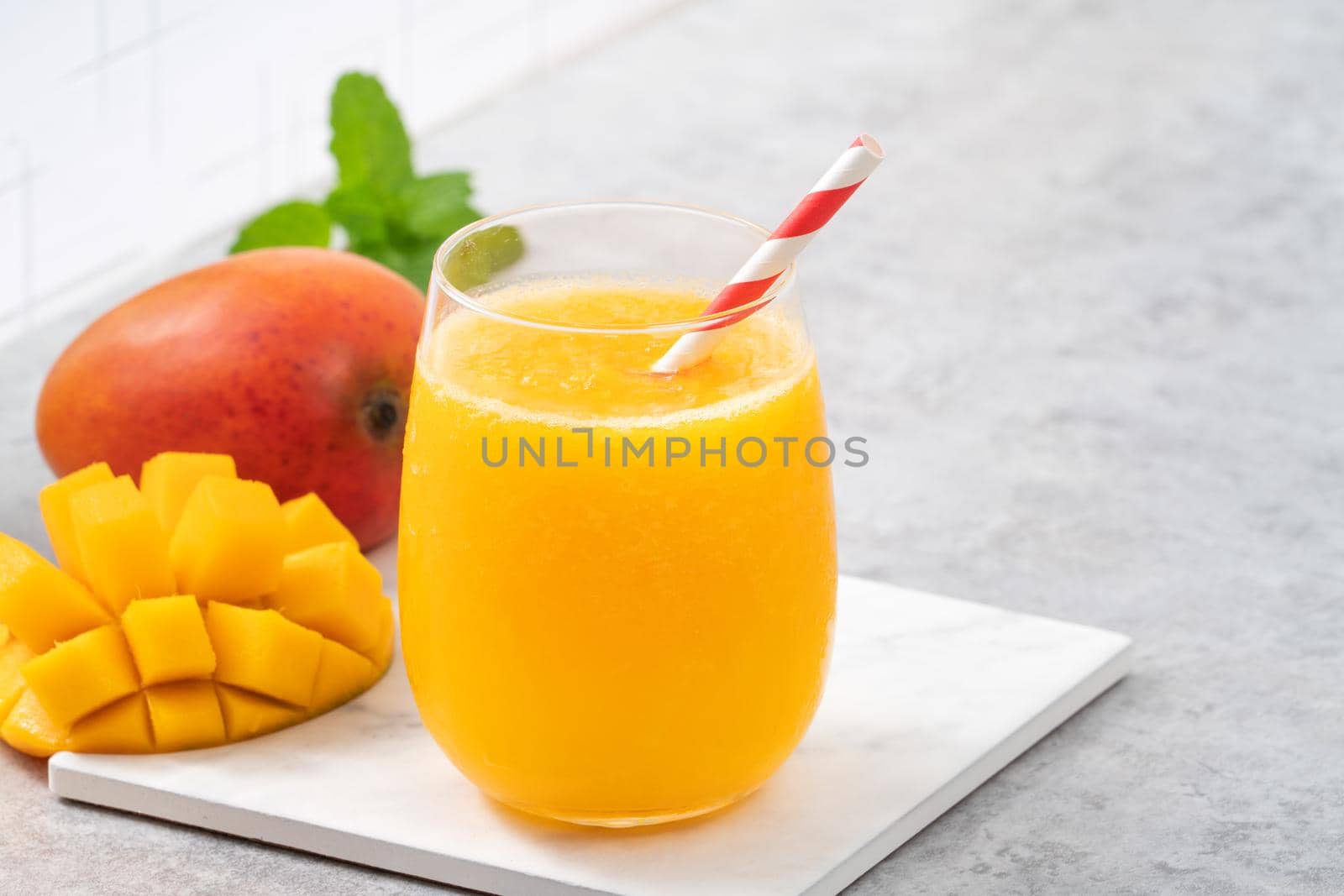 Fresh mango juice. Close up design concept of smoothie cold drink in a glass cup with paper straw on gray table background.