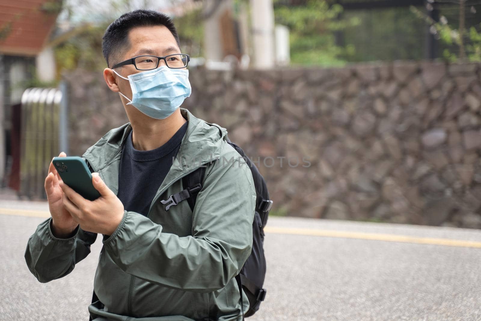 Young backpacker man is traveling alone and using smart phone with wearing mask, glasses. by ROMIXIMAGE