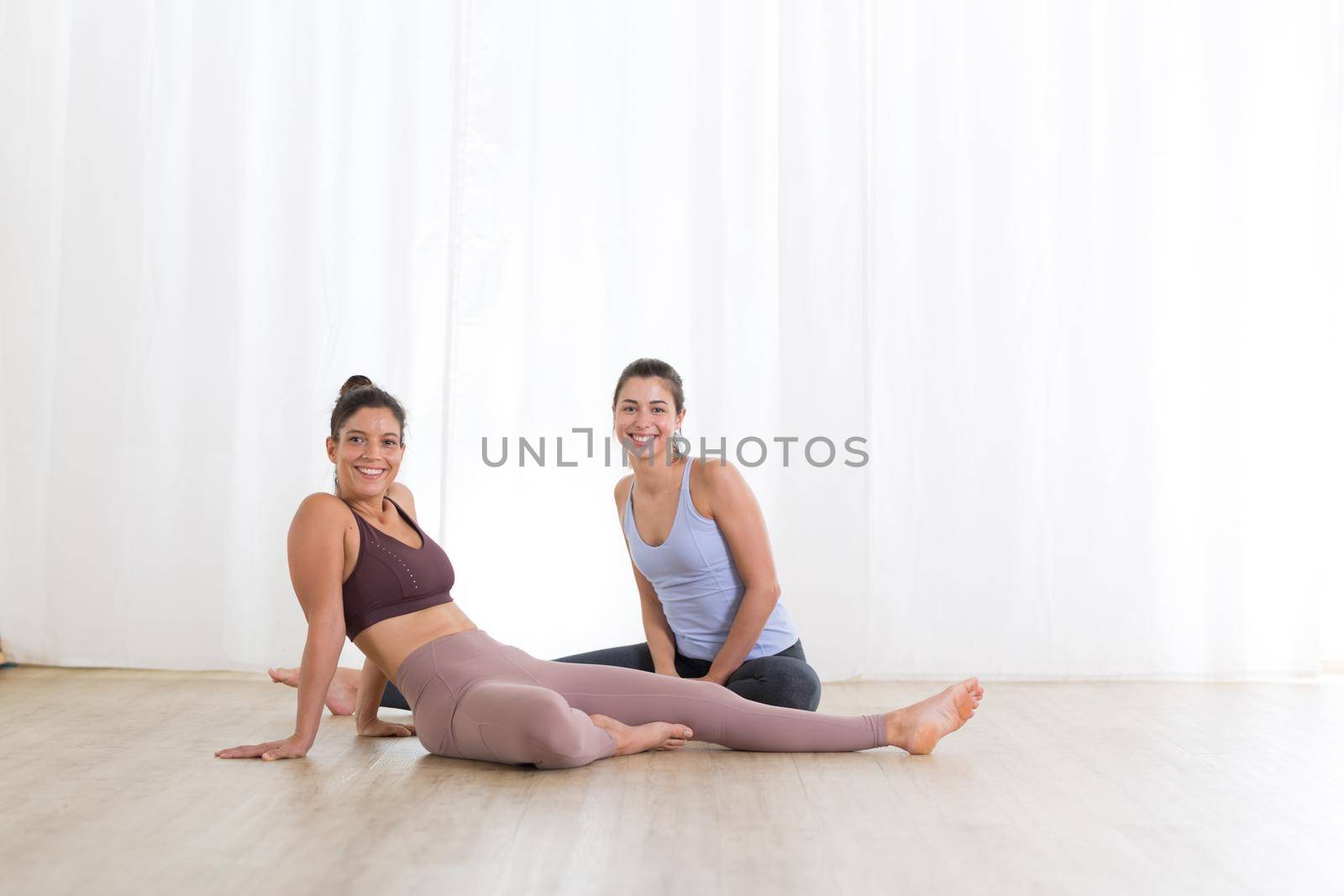 Portrait of active sporty young women relaxing after yoga session in studio. Healthy active lifestyle, working out indoors in gym by kasto