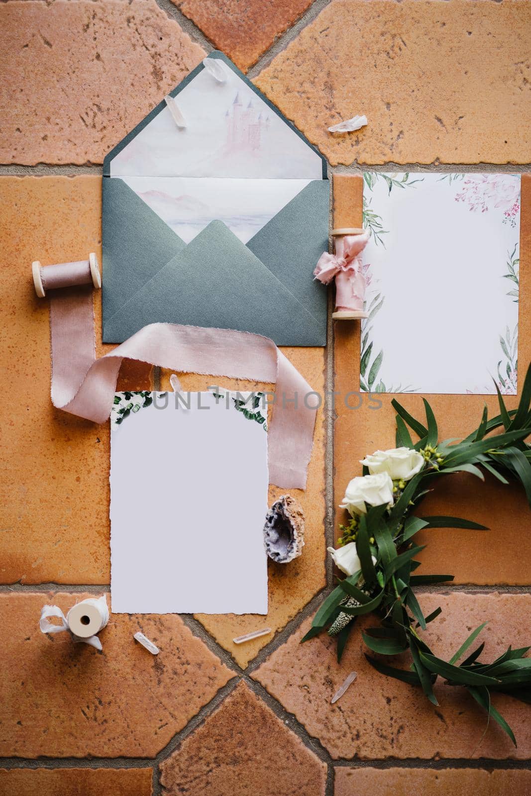 On a brown tile - an open gray envelope, blank postcards with ornaments, skeins of ribbons, a shell and a wreath of twigs with a rose. High quality photo