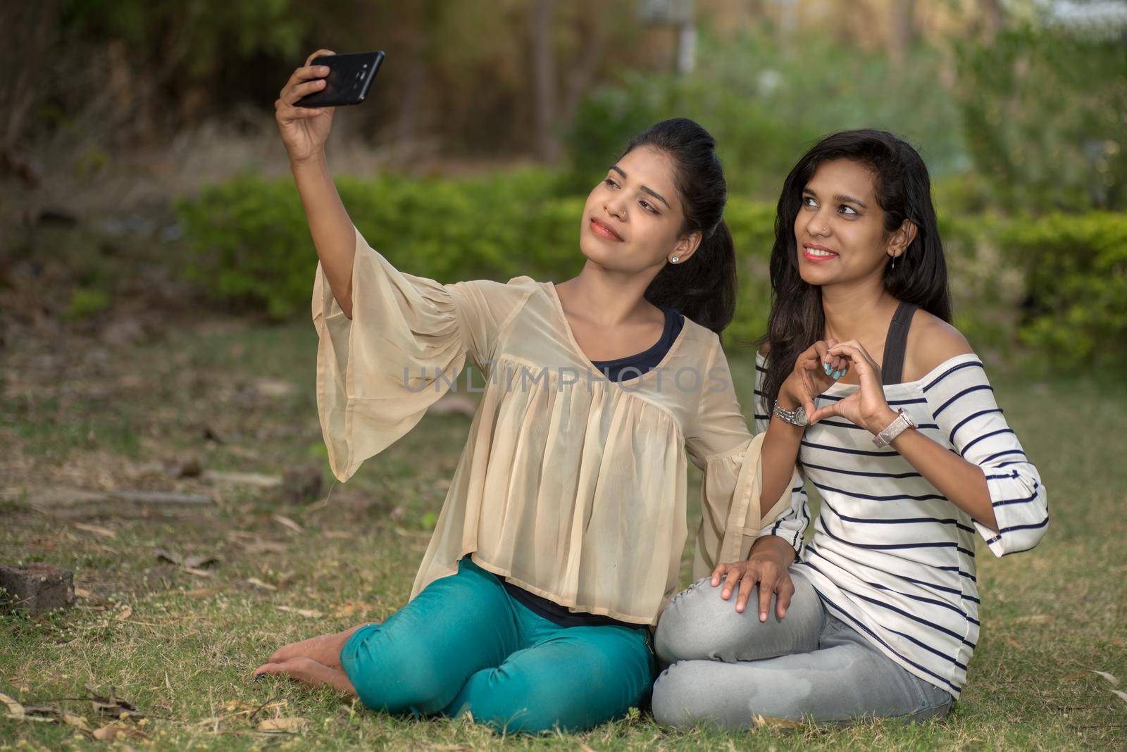 Two beautiful female friends taking selfie with smartphone in outdoors.