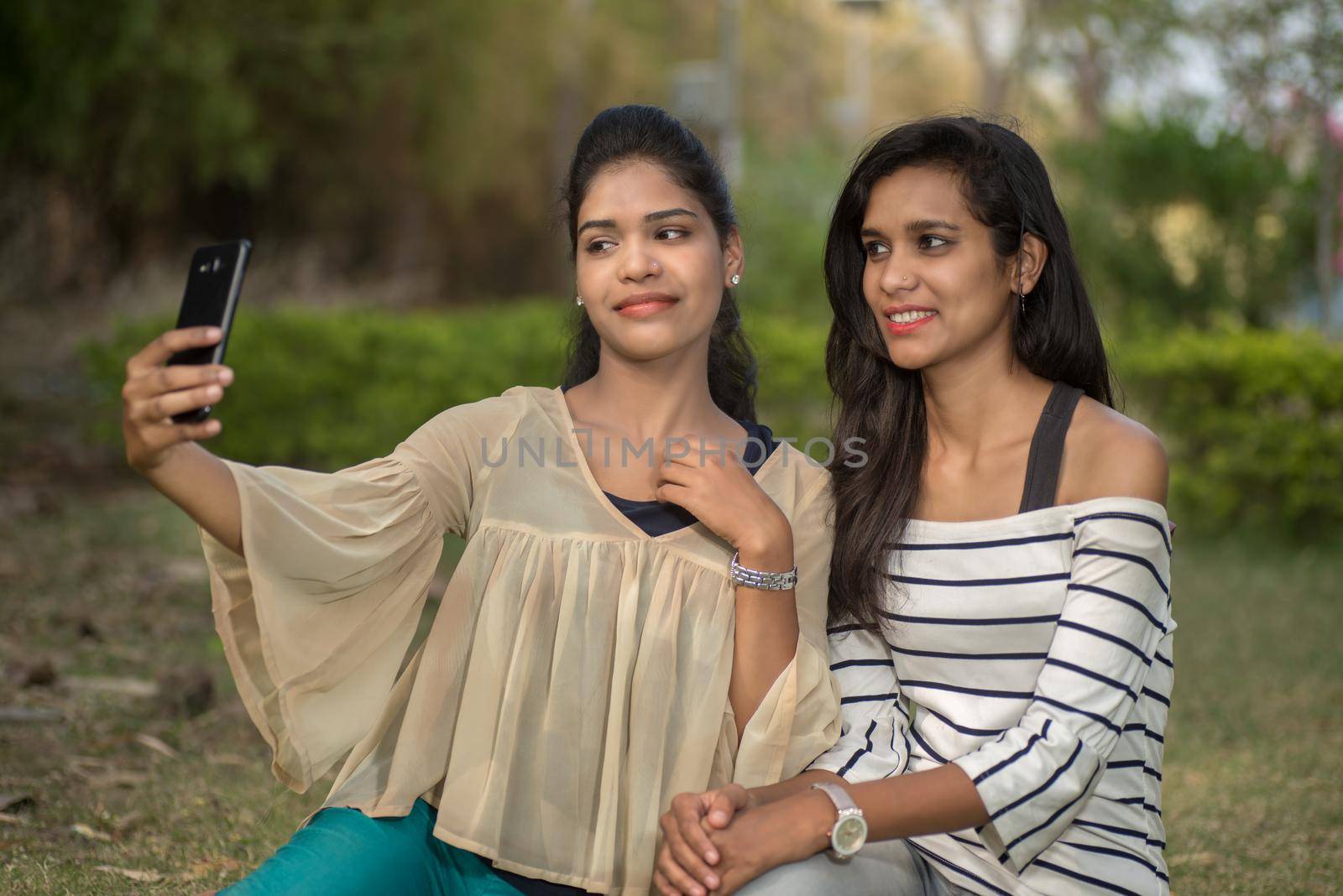 Two beautiful female friends taking selfie with smartphone in outdoors. by DipakShelare