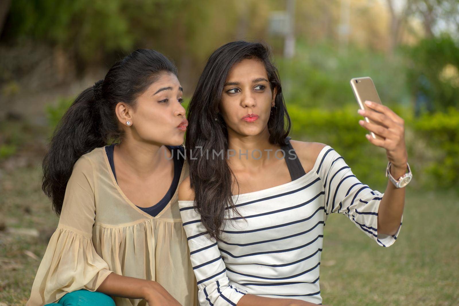 Two beautiful female friends taking selfie with smartphone in outdoors.