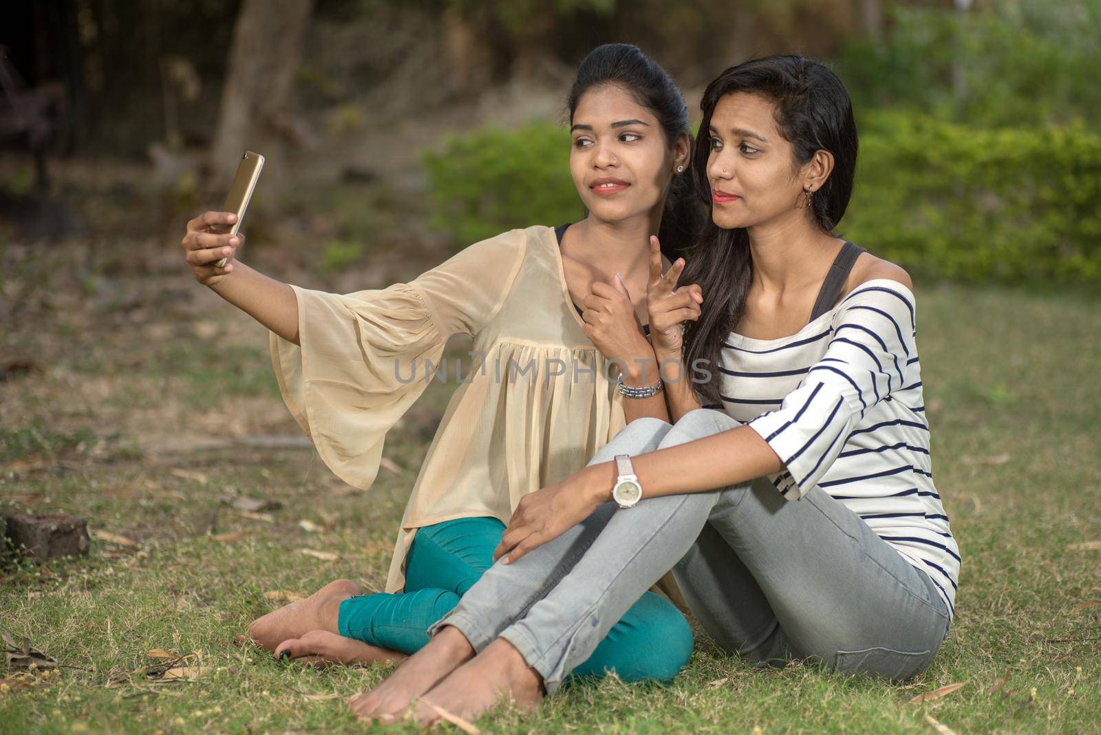 Two beautiful female friends taking selfie with smartphone in outdoors.