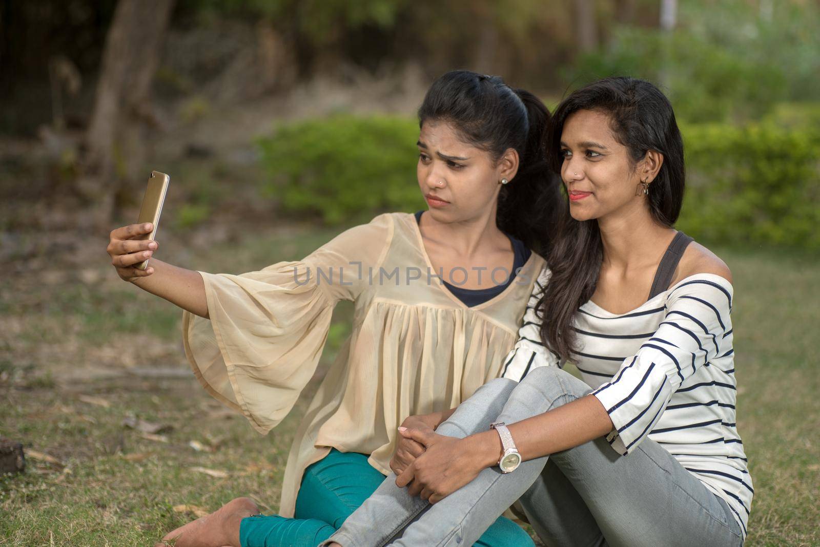 Two beautiful female friends taking selfie with smartphone in outdoors.