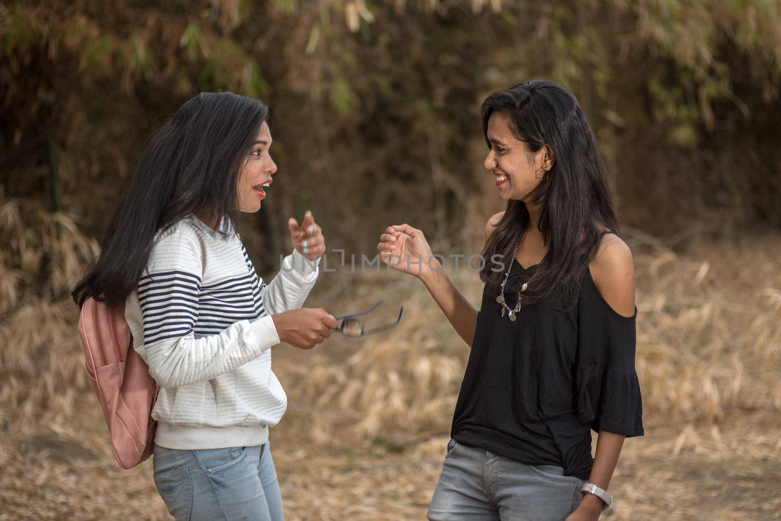 Two young girl friends standing together and having fun in outdoors. Looking at camera.