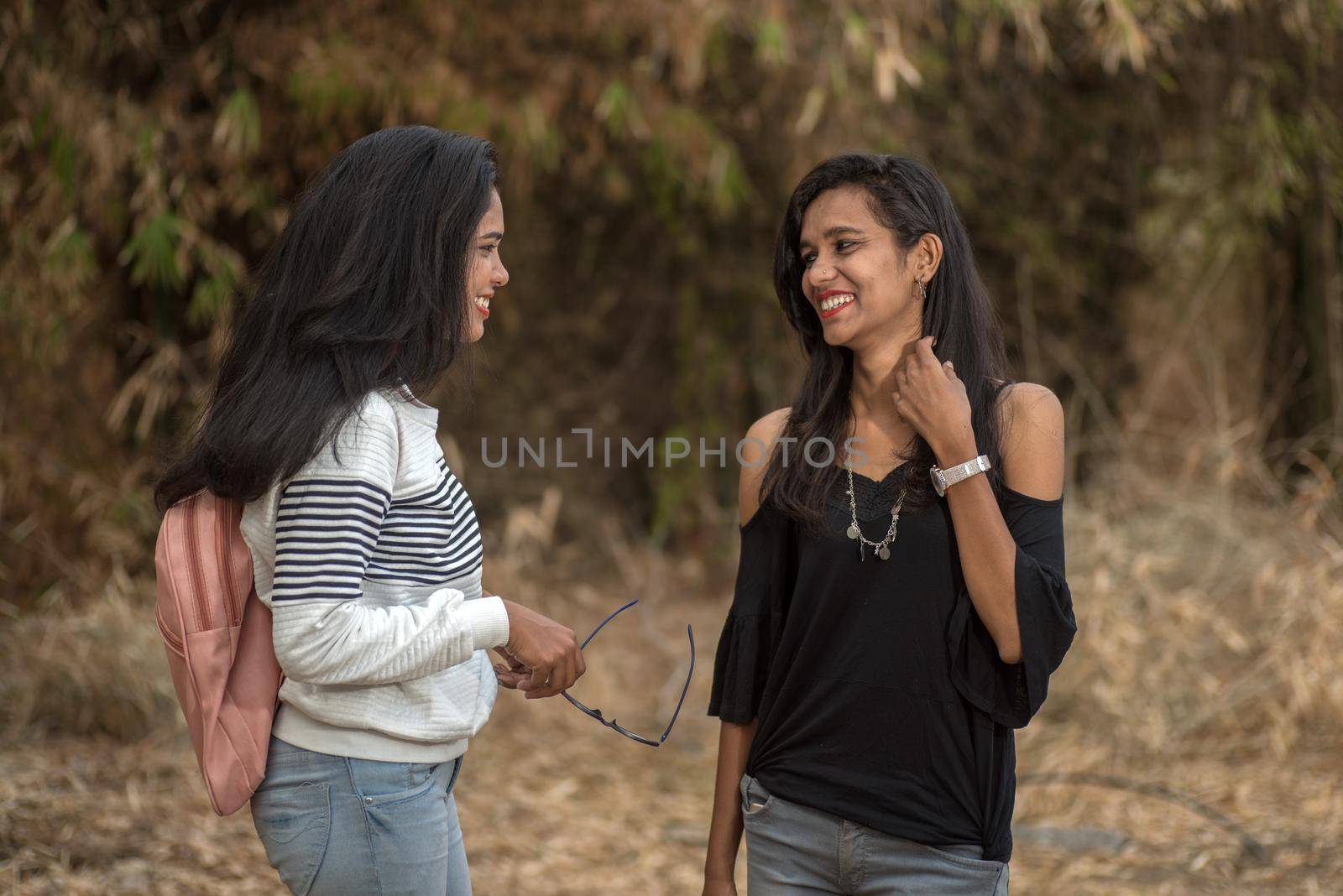 Two young girl friends standing together and having fun in outdoors. Looking at camera.