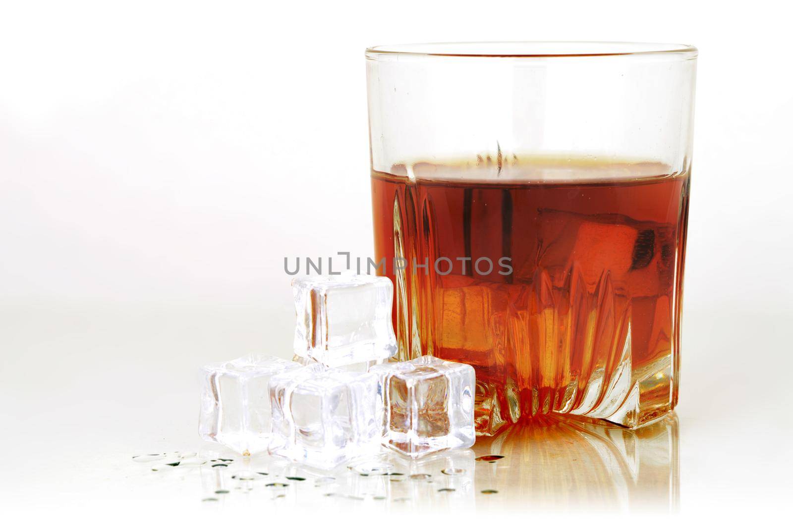 A cold glass of whiskey served with ice over a smoky grey and white background.
