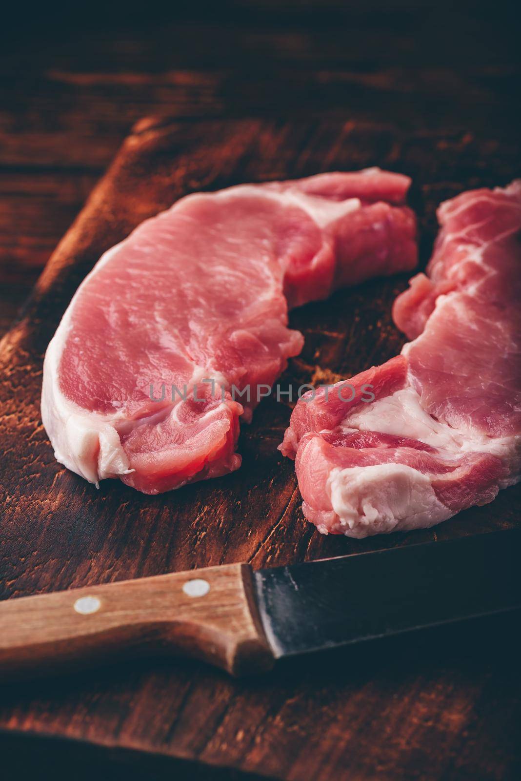 Two pork loin steaks with knife on rustic cutting board