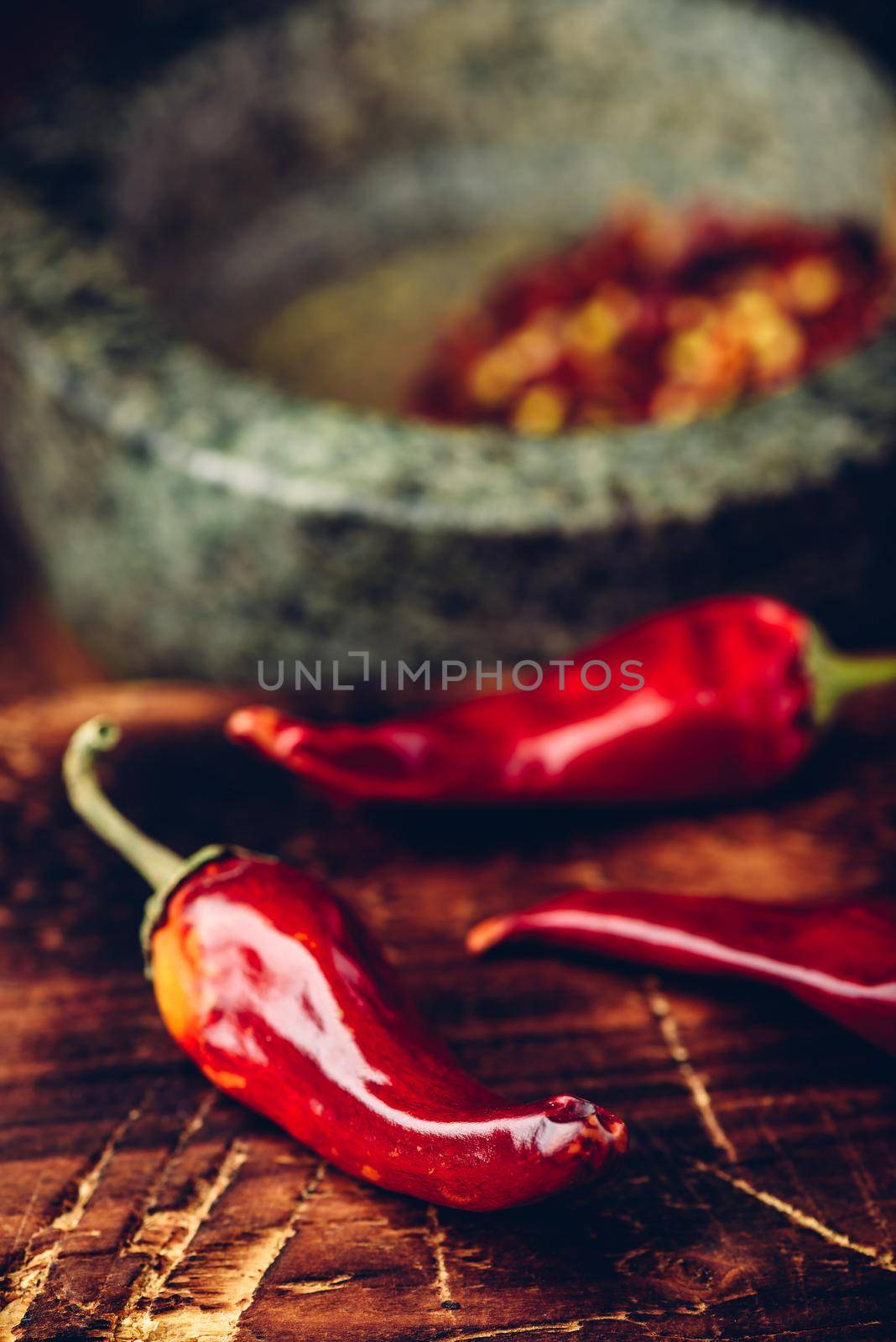 Sun dried red chili peppers on wooden surface with mortar and pestle