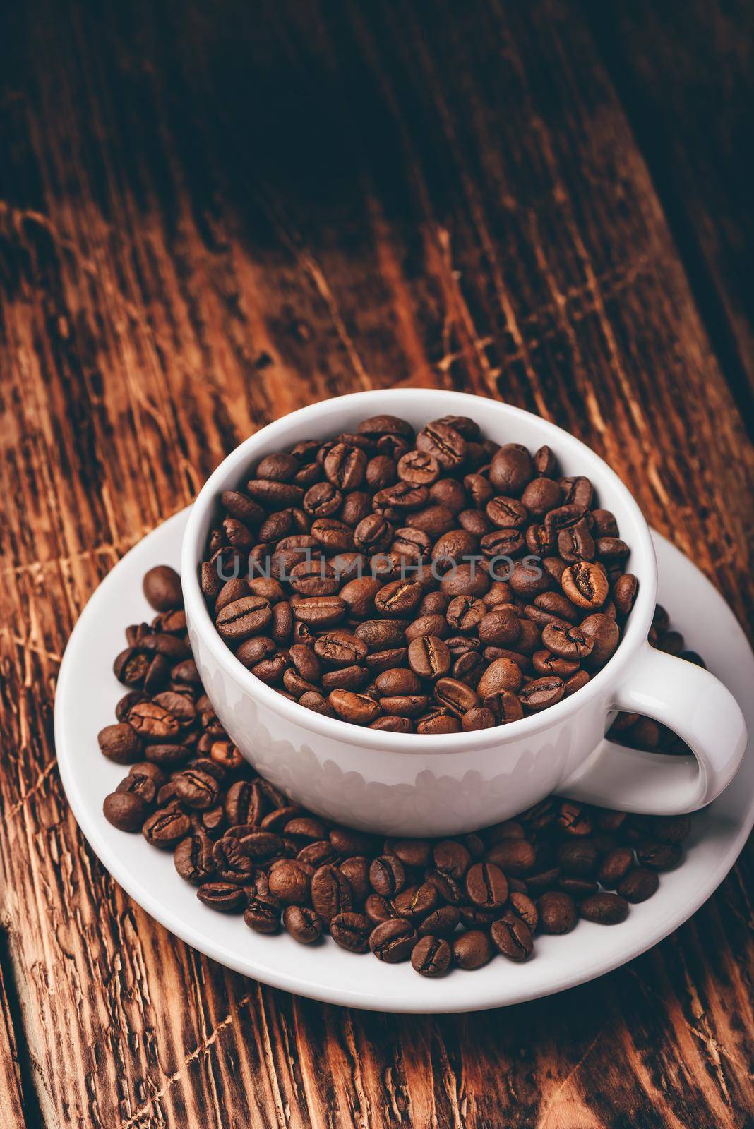 White cup full of roasted coffee beans on saucer