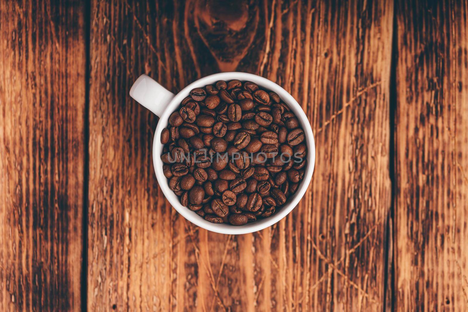 Roasted coffee beans in white cup over rustic wooden surface