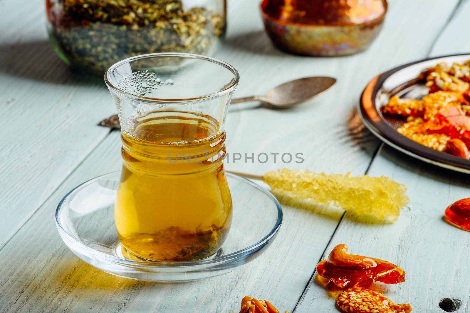 Herbal tea in armudu glass with arabic delights on metal plate over light wooden surface