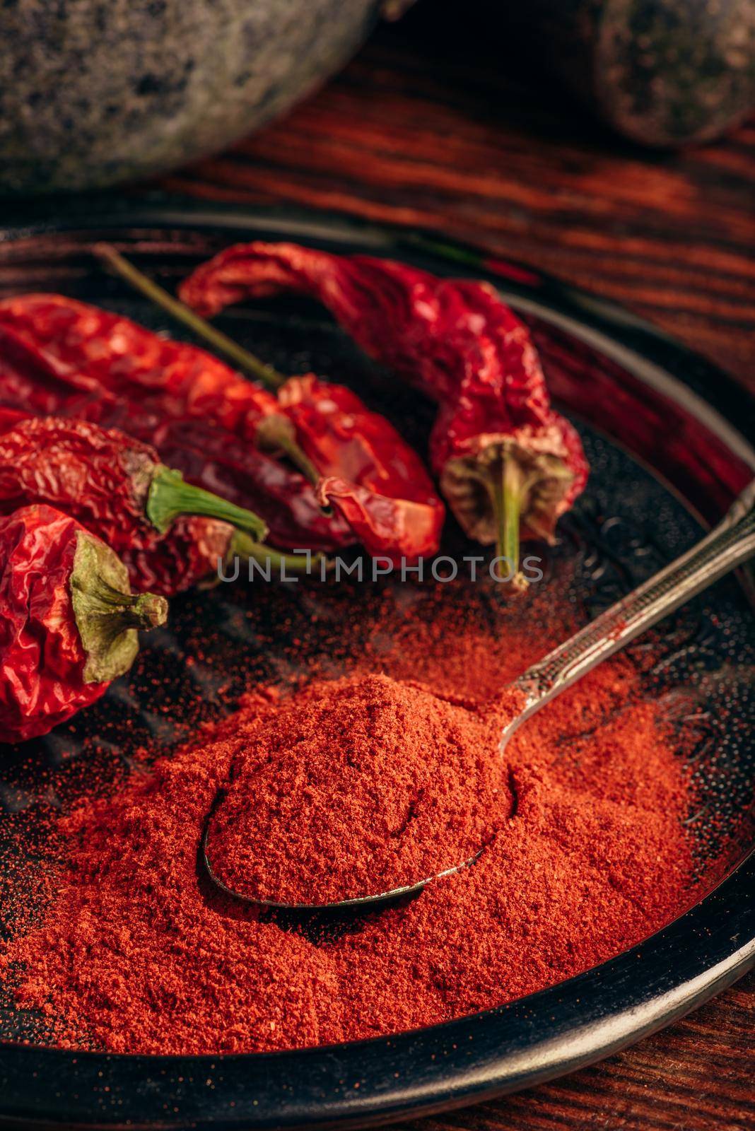 Spoonful of ground chili pepper with dried fruits on metal plate