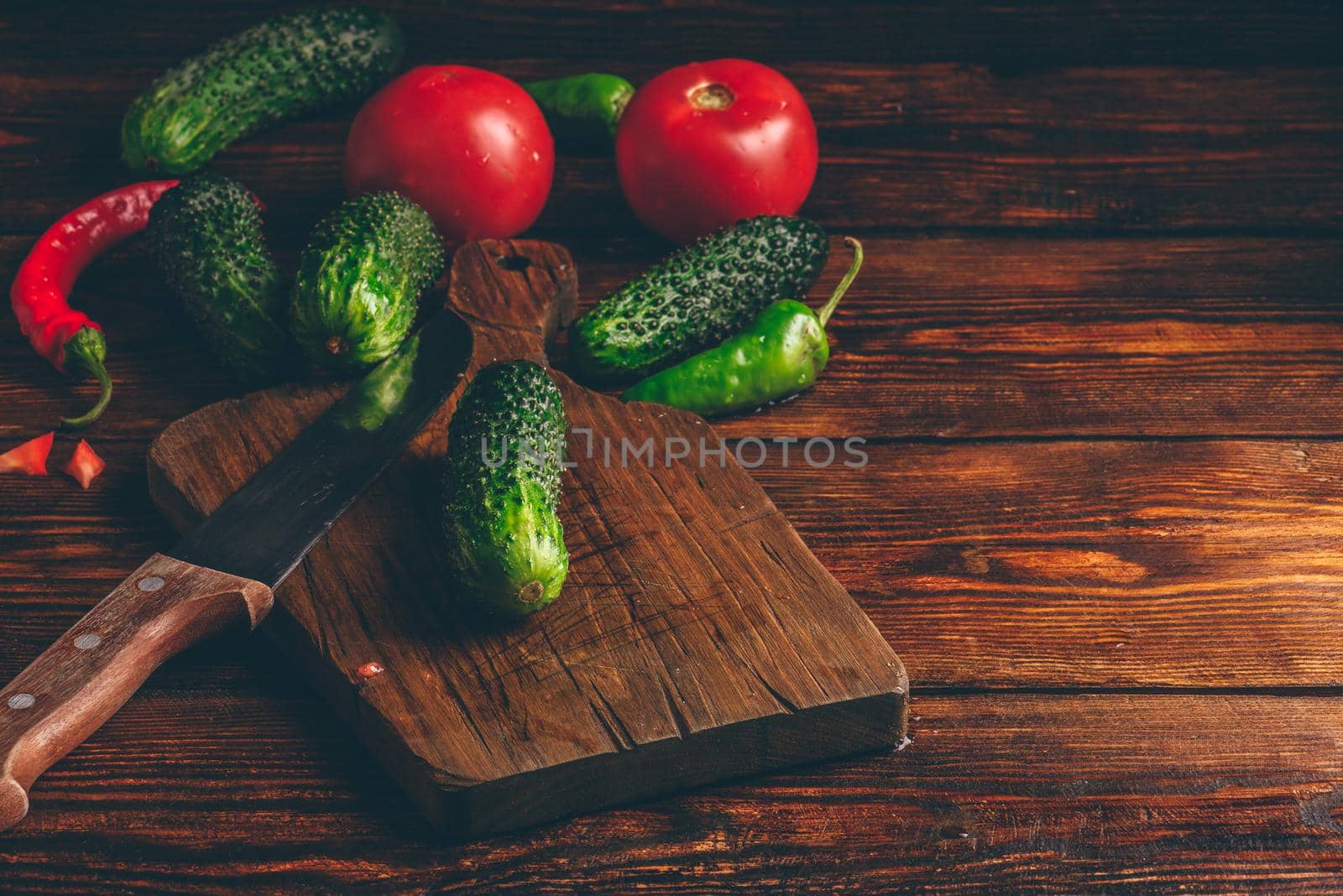 Fresh cucumbers, tomatoes and chili peppers on cutting board for preparing salad.