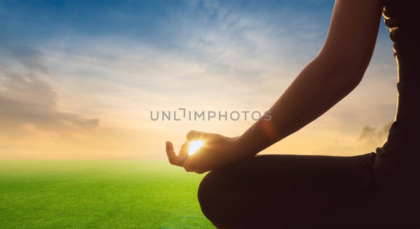 Young woman practice yoga lotus pose to meditation on green field background. Health Concept.