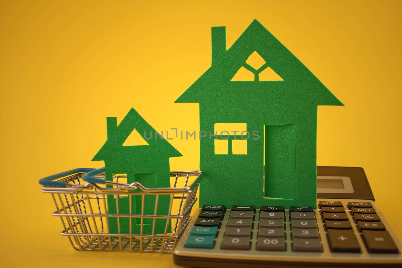Buying a bigger or smaller houses concept with two different sizes of houses, shopping cart and calculator on yellow background