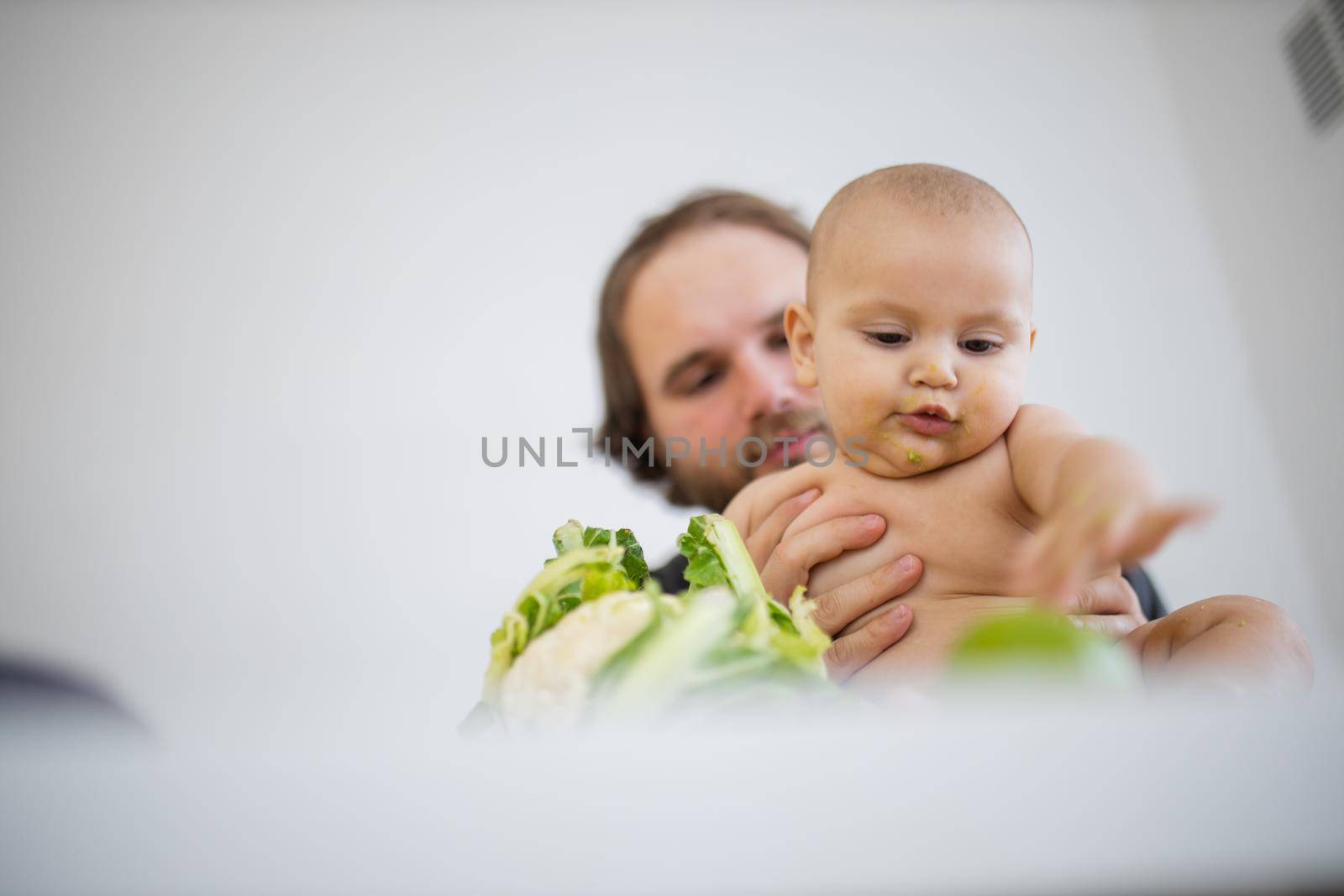 Father lovingly holding and kissing his baby daughter above a table by Kanelbulle